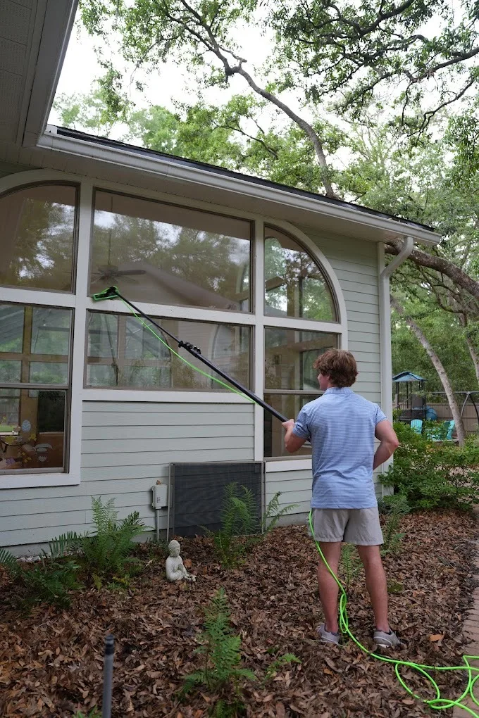 Technician cleaning tall arched sunroom windows with a water-fed pole